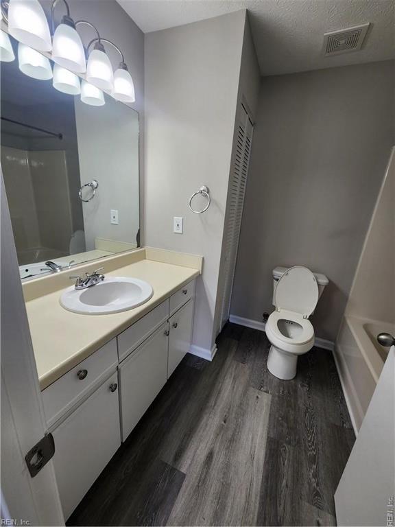 full bathroom with vanity, hardwood / wood-style floors, a textured ceiling, toilet, and shower / bathing tub combination