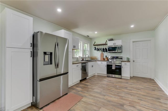 kitchen featuring sink, light wood-type flooring, ornamental molding, appliances with stainless steel finishes, and white cabinetry