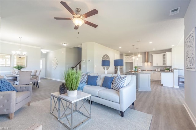 living room with sink, light hardwood / wood-style floors, ceiling fan with notable chandelier, and ornamental molding