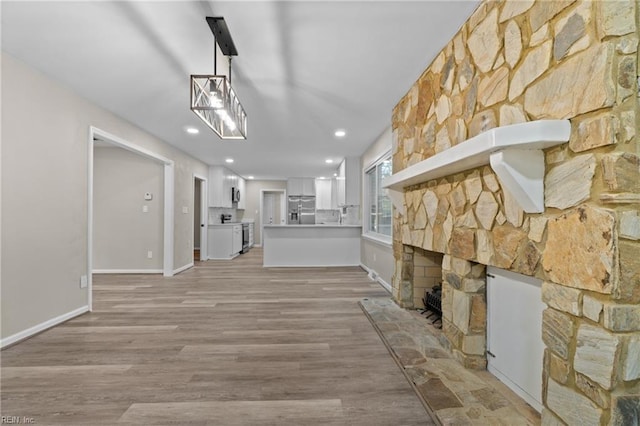 interior space with a stone fireplace, hanging light fixtures, appliances with stainless steel finishes, white cabinetry, and kitchen peninsula