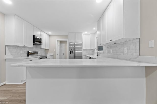 kitchen featuring sink, white cabinetry, light stone counters, kitchen peninsula, and stainless steel appliances