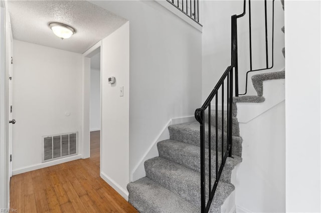 stairs with hardwood / wood-style floors and a textured ceiling