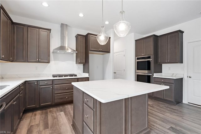 kitchen with stainless steel appliances, dark wood-type flooring, wall chimney range hood, decorative light fixtures, and a center island