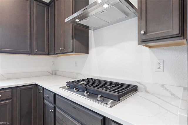 kitchen with light stone countertops, dark brown cabinets, stainless steel gas cooktop, and wall chimney exhaust hood