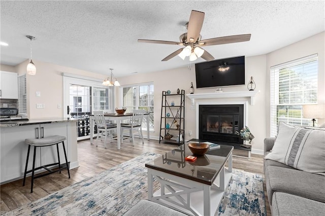 living room featuring ceiling fan with notable chandelier, light wood-type flooring, and a textured ceiling