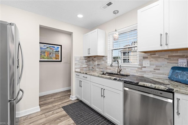 kitchen featuring pendant lighting, sink, light stone counters, white cabinetry, and stainless steel appliances