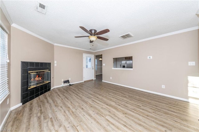 unfurnished living room featuring crown molding, ceiling fan, light wood-type flooring, a textured ceiling, and a tiled fireplace