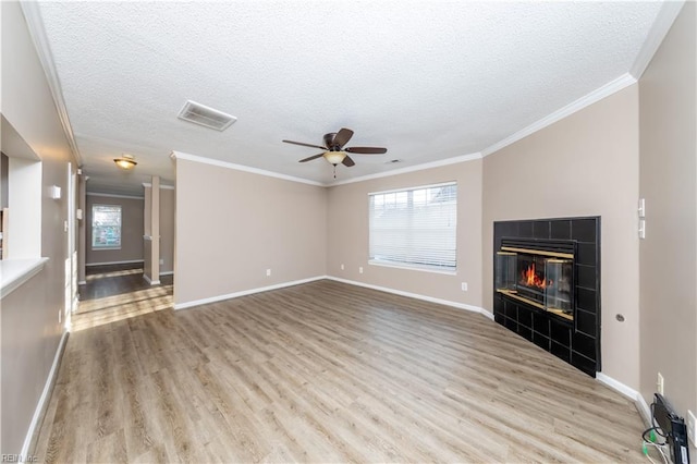 unfurnished living room featuring a tile fireplace, ceiling fan, light hardwood / wood-style flooring, a textured ceiling, and ornamental molding