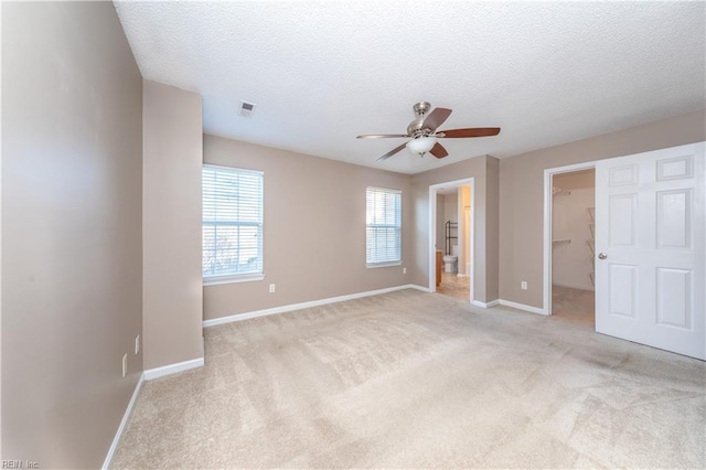 unfurnished bedroom with a walk in closet, ceiling fan, a closet, and light carpet