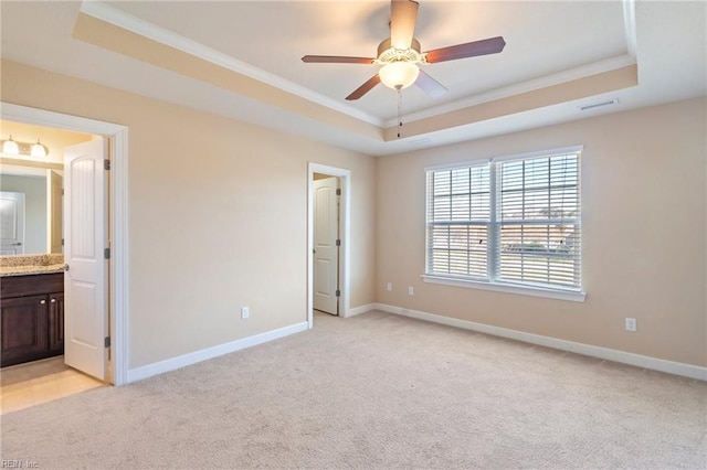 unfurnished bedroom featuring light carpet, a raised ceiling, ceiling fan, ornamental molding, and connected bathroom