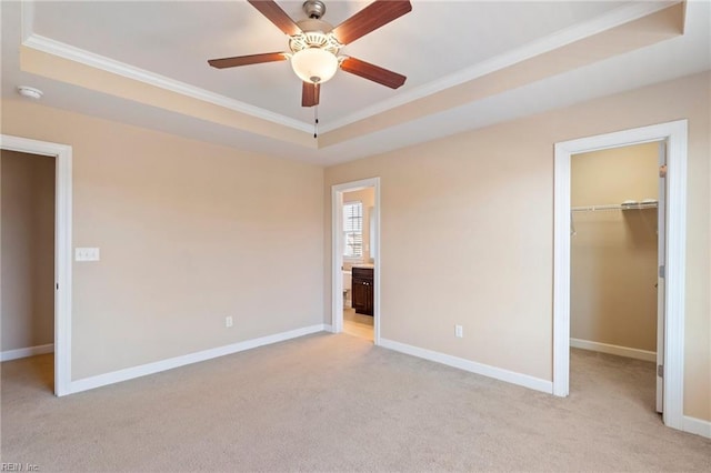 unfurnished bedroom featuring a walk in closet, crown molding, ceiling fan, a tray ceiling, and a closet