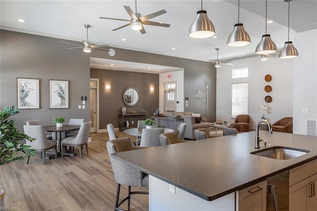 kitchen with sink, light hardwood / wood-style floors, decorative light fixtures, a center island with sink, and ornamental molding