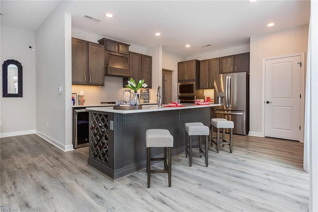 kitchen featuring premium range hood, a kitchen island with sink, stainless steel refrigerator with ice dispenser, built in microwave, and a breakfast bar area