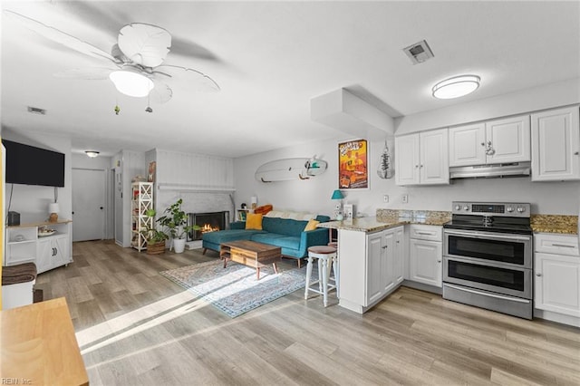 kitchen featuring double oven range, light stone countertops, a fireplace, white cabinetry, and kitchen peninsula