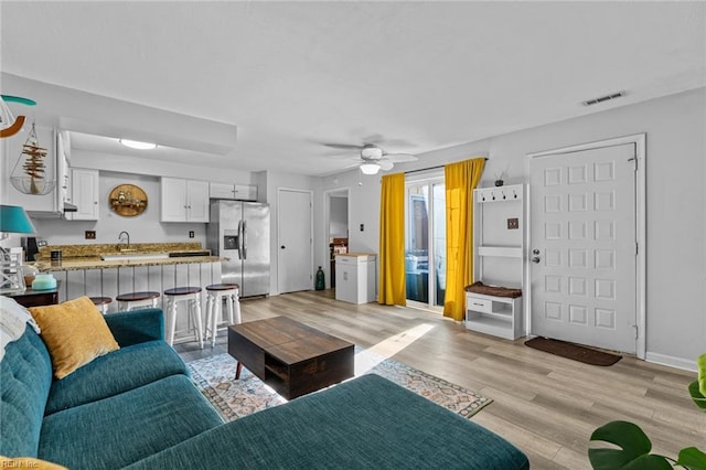 living room with light wood-type flooring, ceiling fan, and sink