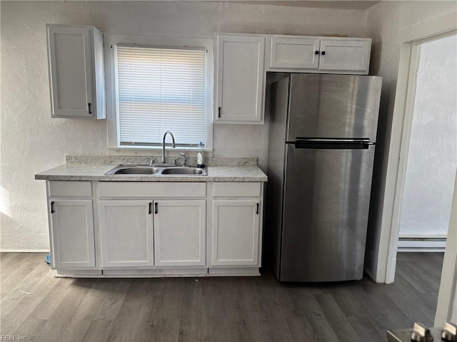 kitchen featuring wood-type flooring, stainless steel fridge, white cabinetry, and sink