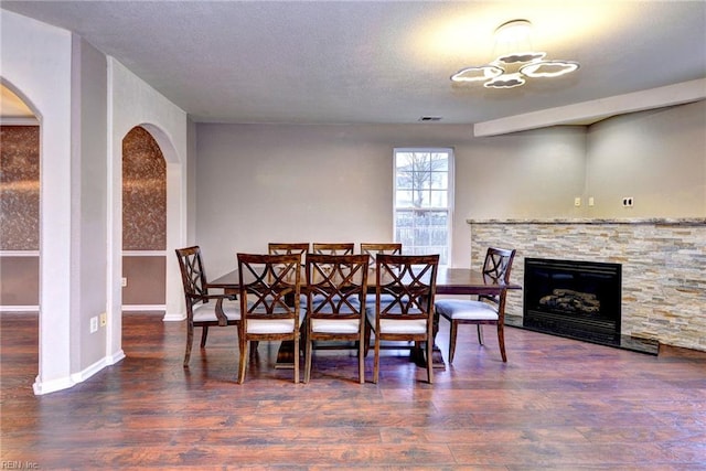 dining room with a textured ceiling, an inviting chandelier, dark hardwood / wood-style floors, and a stone fireplace