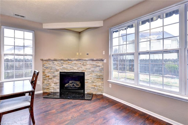 living room featuring beam ceiling, a stone fireplace, and dark wood-type flooring