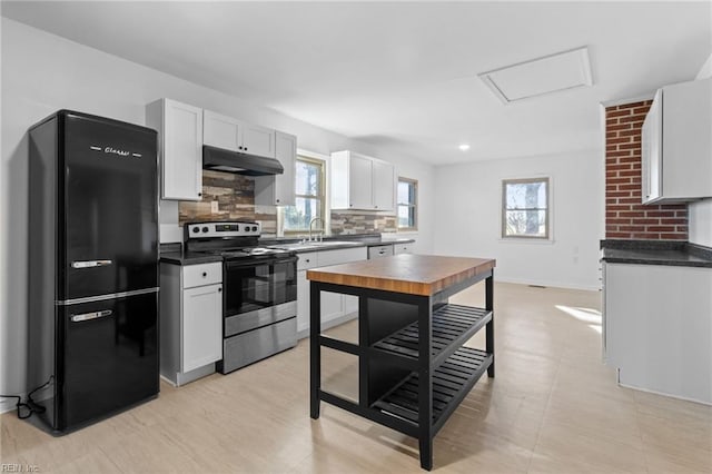 kitchen with black refrigerator, backsplash, sink, white cabinetry, and stainless steel electric range