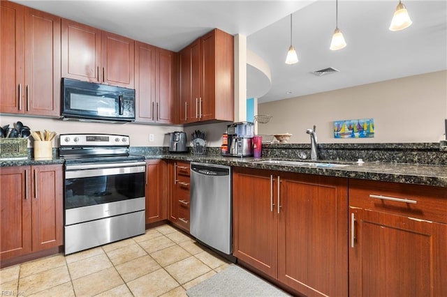 kitchen featuring appliances with stainless steel finishes, dark stone counters, sink, light tile patterned floors, and hanging light fixtures