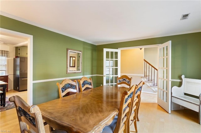 dining space featuring crown molding, light hardwood / wood-style flooring, and french doors