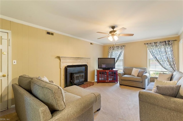 living room featuring a wood stove, ceiling fan, crown molding, and carpet