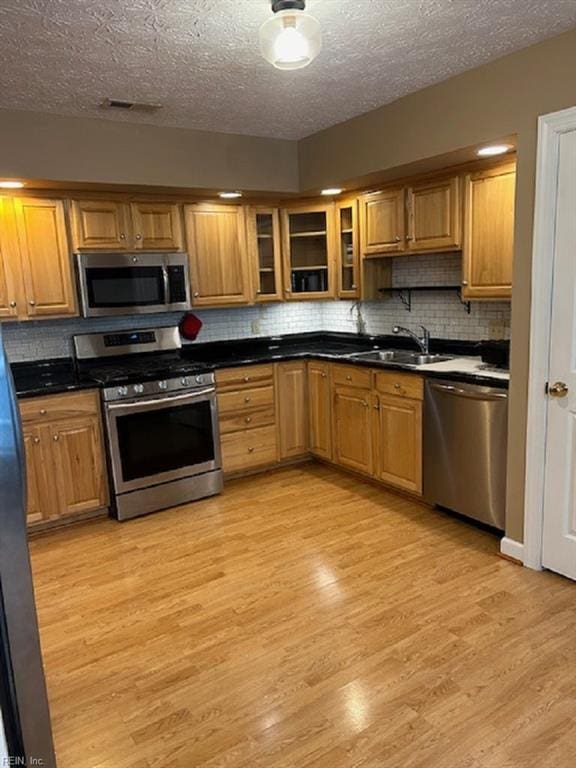 kitchen with decorative backsplash, appliances with stainless steel finishes, light wood-type flooring, a textured ceiling, and sink