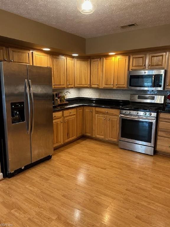 kitchen featuring a textured ceiling, stainless steel appliances, and light hardwood / wood-style flooring