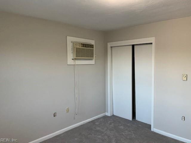 unfurnished bedroom with dark carpet, a wall unit AC, and a closet