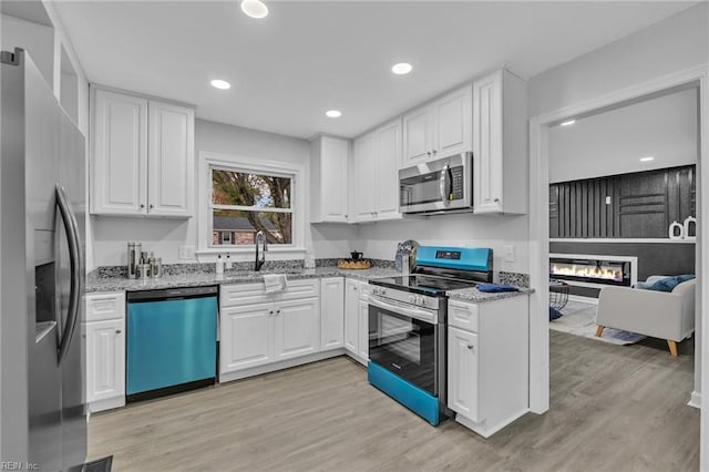 kitchen with white cabinets, sink, light stone countertops, and stainless steel appliances