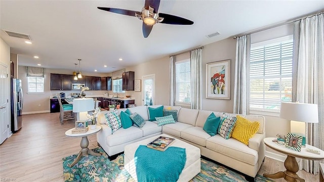 living room featuring a wealth of natural light, light hardwood / wood-style flooring, ceiling fan, and sink