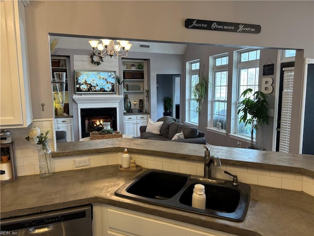 kitchen featuring backsplash, white cabinets, sink, stainless steel dishwasher, and a chandelier