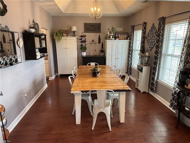 dining space with a raised ceiling, dark wood-type flooring, and an inviting chandelier