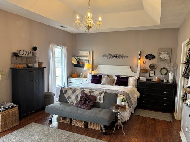 bedroom with a raised ceiling, dark wood-type flooring, and a notable chandelier