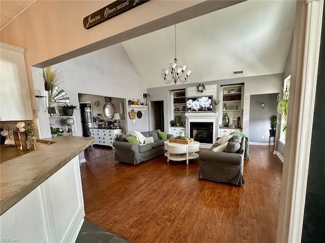 living room featuring dark wood-type flooring, built in features, high vaulted ceiling, and a chandelier