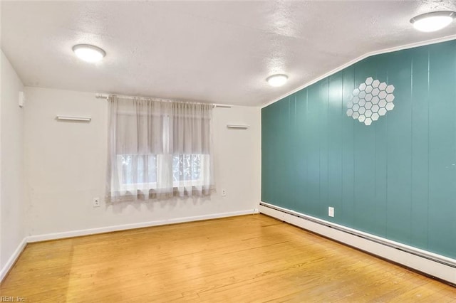 spare room featuring wood-type flooring, a textured ceiling, vaulted ceiling, and baseboard heating