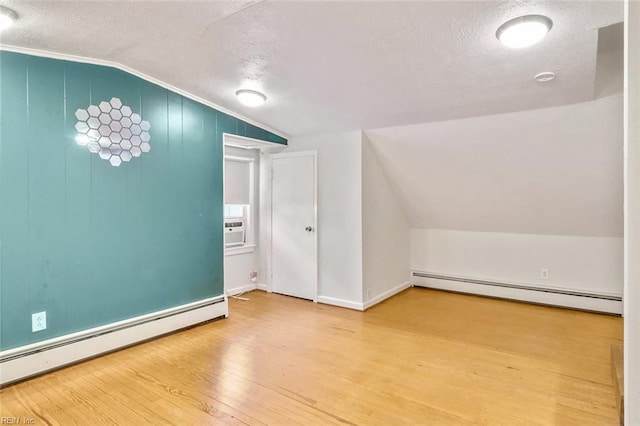 additional living space with baseboard heating, hardwood / wood-style floors, a textured ceiling, and vaulted ceiling