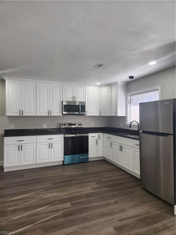 kitchen featuring appliances with stainless steel finishes, sink, pendant lighting, dark hardwood / wood-style floors, and white cabinetry