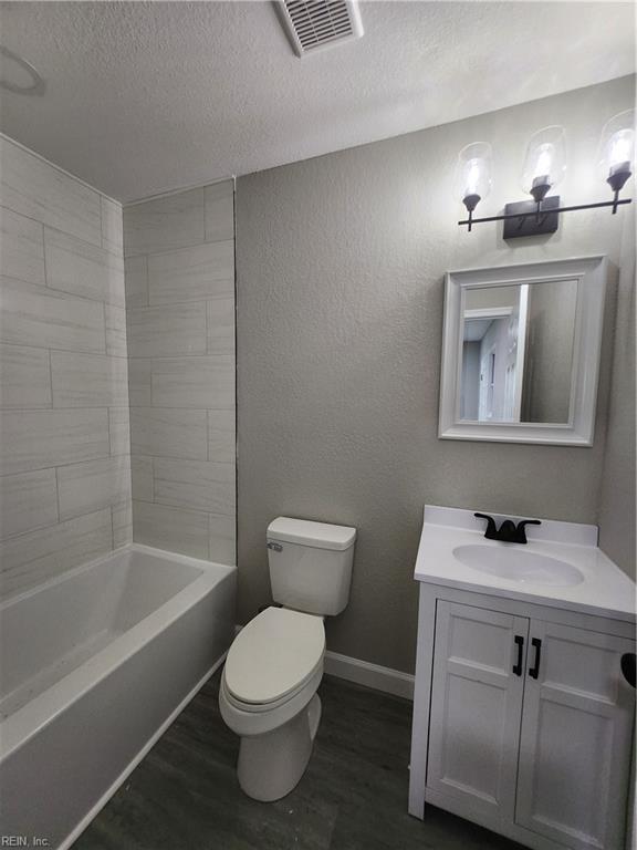 full bathroom featuring a textured ceiling, toilet, hardwood / wood-style flooring, vanity, and tiled shower / bath