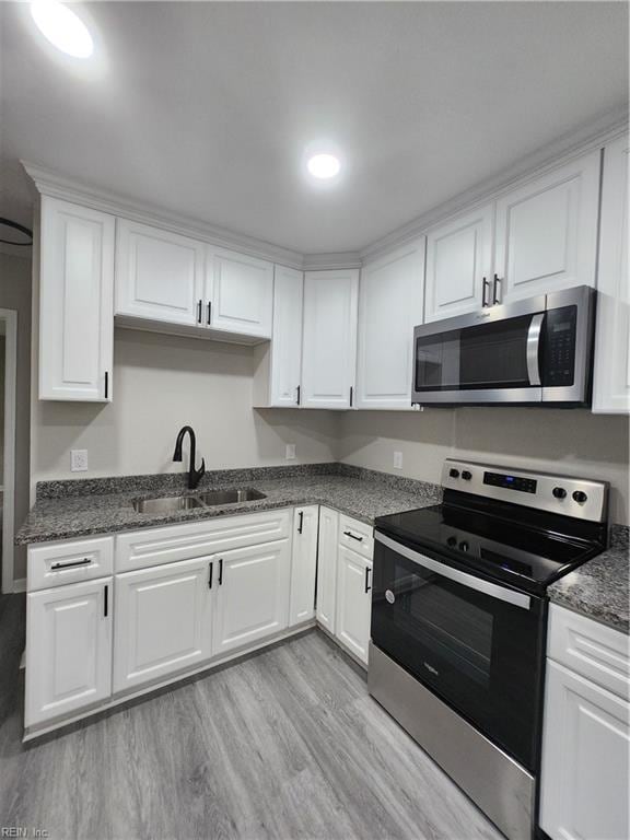 kitchen with dark stone counters, stainless steel appliances, sink, light hardwood / wood-style flooring, and white cabinetry