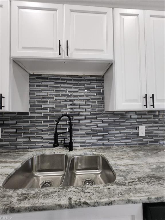 interior details featuring tasteful backsplash, light stone countertops, sink, and white cabinets