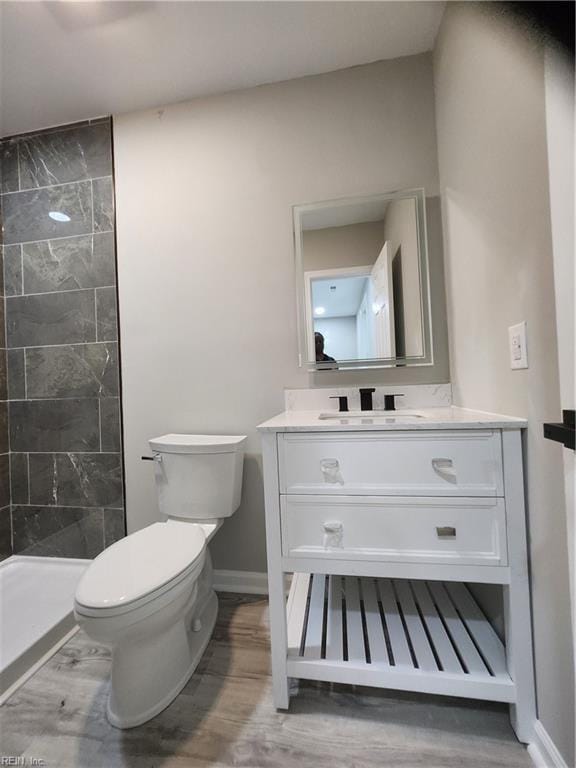 bathroom featuring hardwood / wood-style flooring, vanity, toilet, and tiled shower