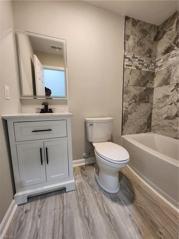 full bathroom featuring tiled shower / bath, hardwood / wood-style flooring, vanity, and toilet