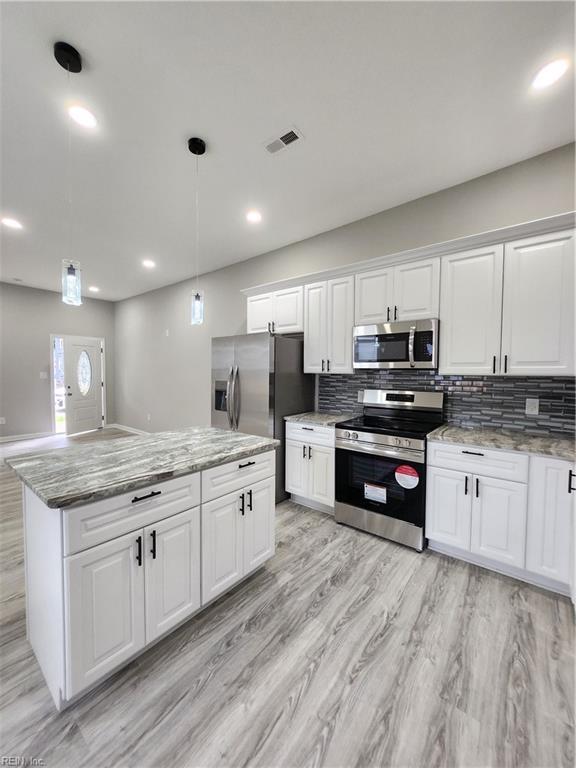 kitchen with white cabinets, appliances with stainless steel finishes, decorative light fixtures, and a kitchen island