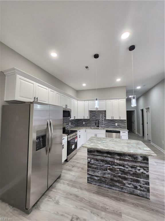 kitchen with white cabinetry, sink, stainless steel appliances, pendant lighting, and light wood-type flooring