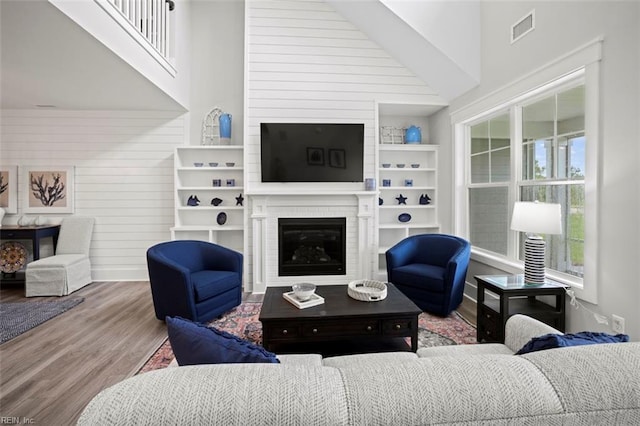 living room featuring built in shelves, a large fireplace, hardwood / wood-style flooring, and high vaulted ceiling