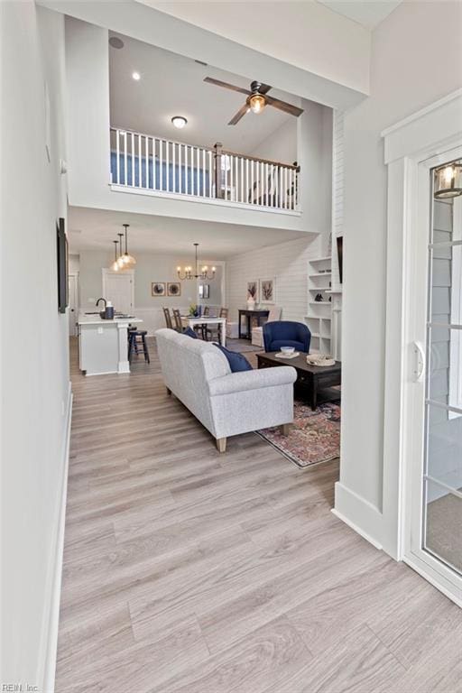 living room with light hardwood / wood-style flooring, a towering ceiling, and ceiling fan with notable chandelier