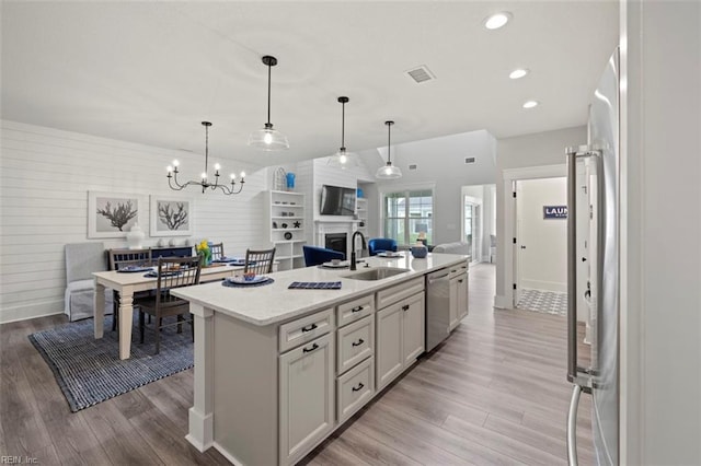 kitchen with sink, stainless steel appliances, light hardwood / wood-style floors, and an island with sink