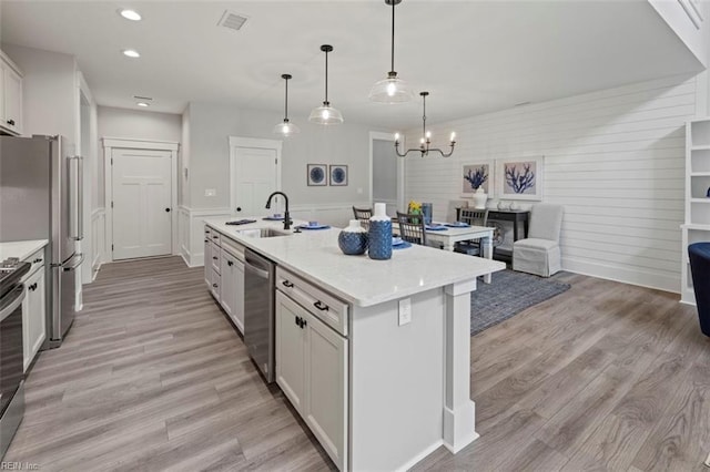 kitchen featuring appliances with stainless steel finishes, a kitchen island with sink, sink, white cabinetry, and hanging light fixtures