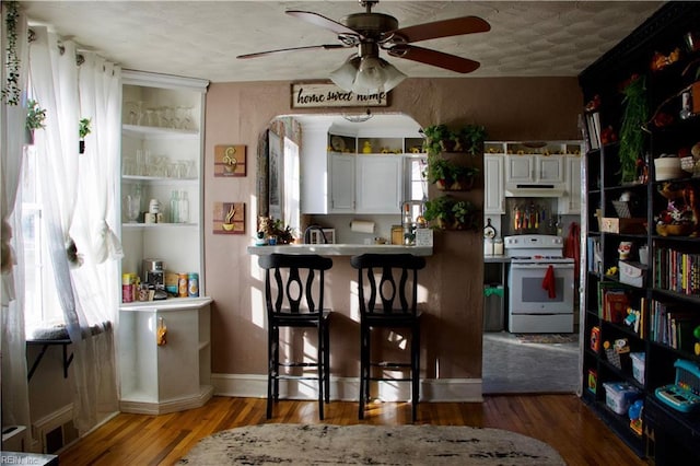 kitchen with white cabinets, a kitchen breakfast bar, ceiling fan, white electric range oven, and wood-type flooring